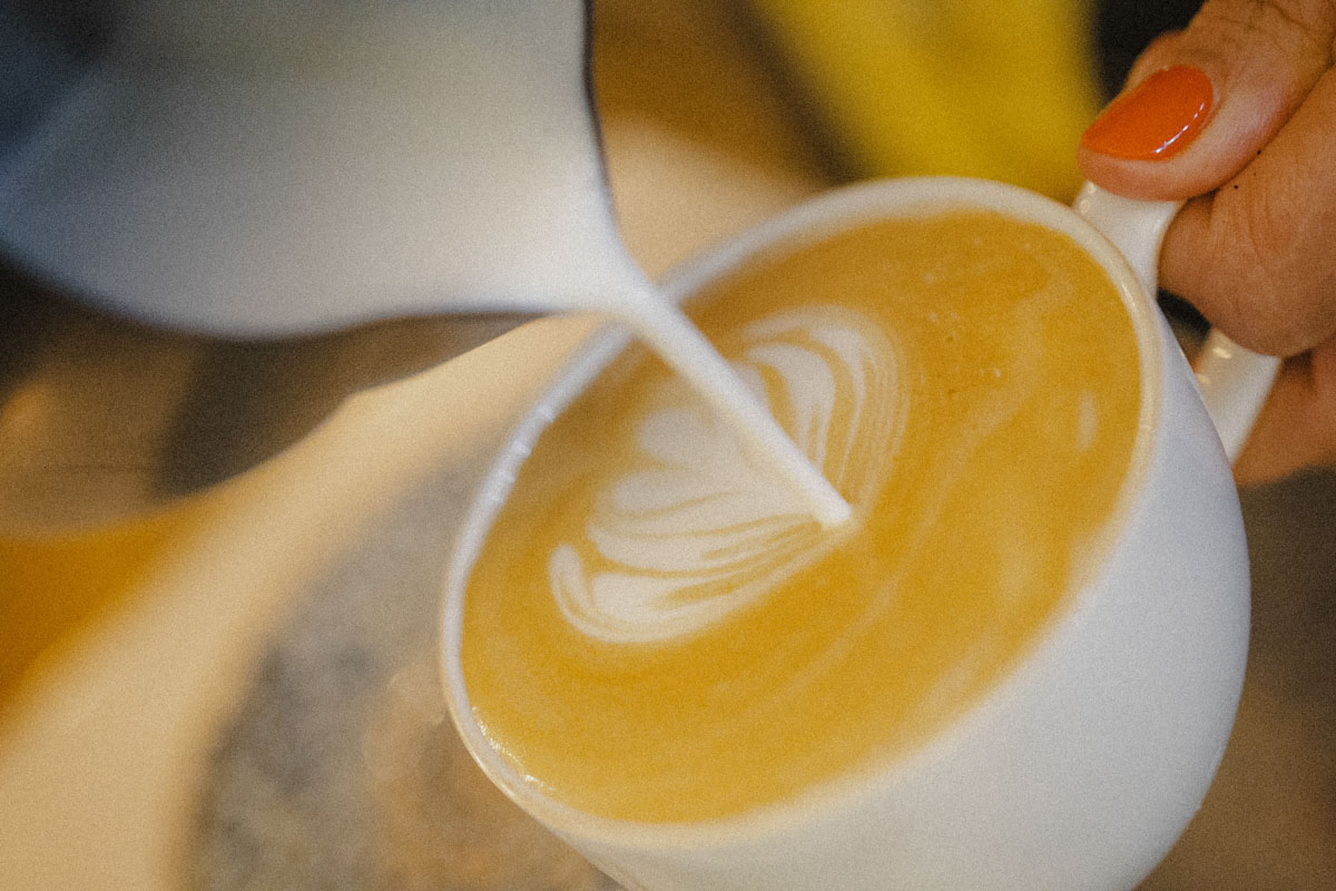 Barista schüttet Milch in Kaffee, sodass ein Herz entsteht